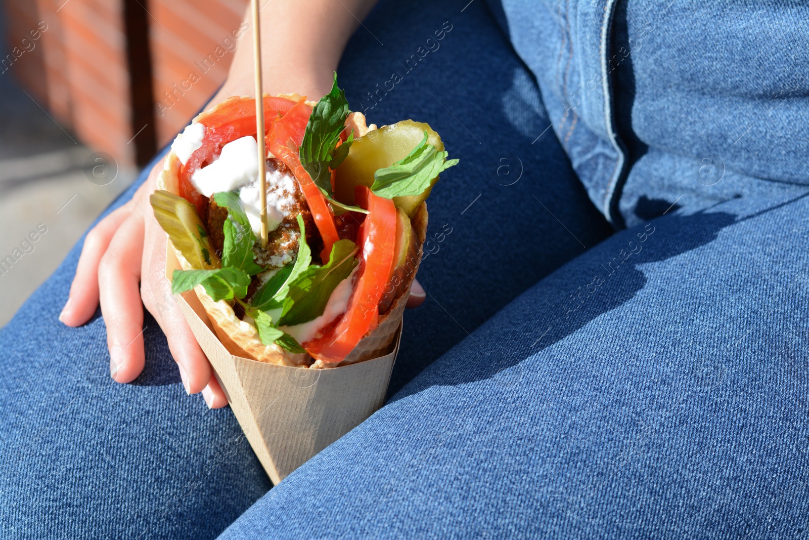 Photo of Woman holding wafer with falafel and vegetables outdoors, closeup. Street food