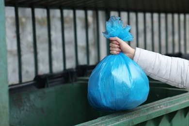 Photo of Woman throwing trash bag full of garbage in bin outdoors, closeup. Space for text