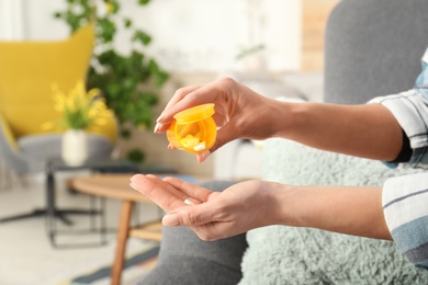 Photo of Woman pouring pills from bottle into hand indoors, closeup