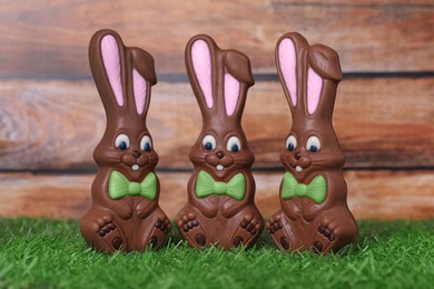 Photo of Easter celebration. Funny chocolate bunnies on grass against wooden background