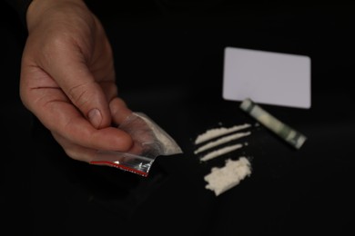 Drug addiction. Man with cocaine and rolled dollar banknote at black table, closeup