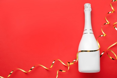 Photo of Bottle of champagne and streamers on red background, flat lay. Space for text