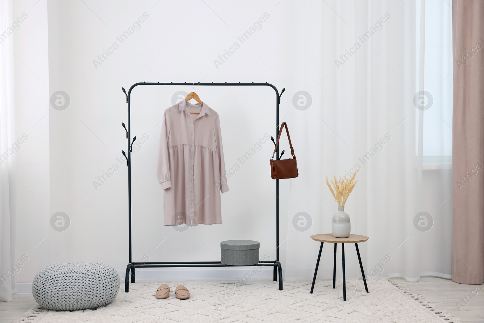 Photo of Clothing rack with stylish dress, bag and shoes in room