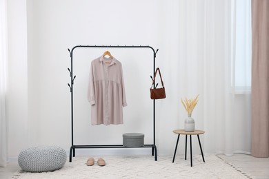 Photo of Clothing rack with stylish dress, bag and shoes in room