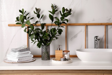 Photo of Vase with green branches, towels and soap dispenser on countertop in bathroom