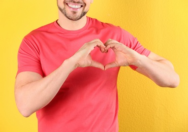 Man making heart with his hands on color background, closeup