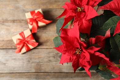 Photo of Poinsettia (traditional Christmas flower) with gift boxes on wooden table, top view