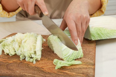 Photo of Woman cutting fresh chinese cabbage at table in kitchen, closeup