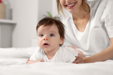 Photo of Cute little baby and mother on cosy bed in room, closeup