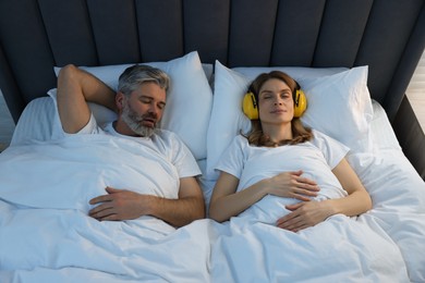 Smiling woman with headphones lying near her snoring husband in bed at home