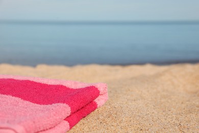 Photo of Soft pink beach towel on sand near sea, space for text