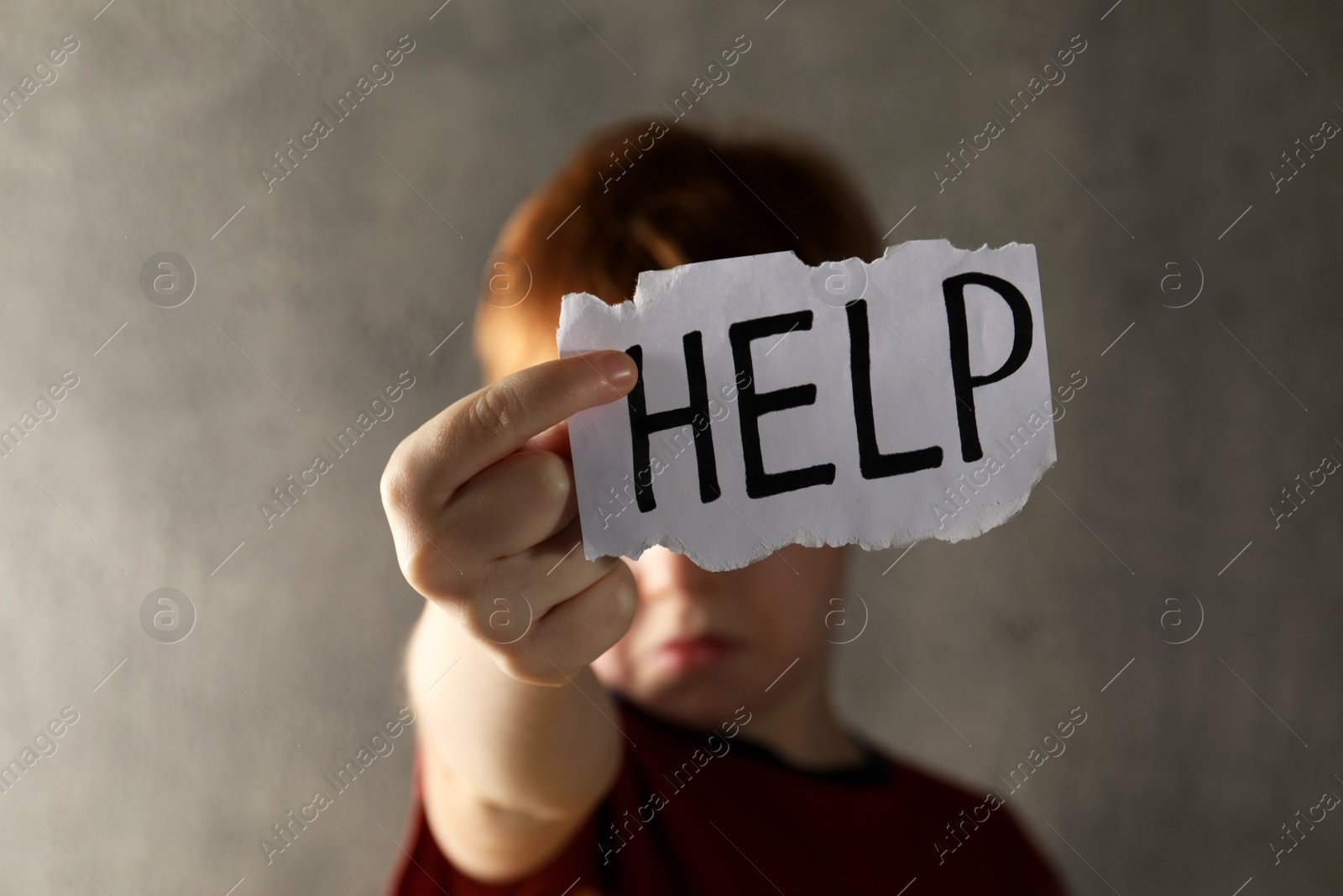 Photo of Little boy holding piece of paper with word Help against light grey background, focus on hand. Domestic violence concept