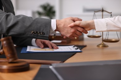 Photo of Notary shaking hands with client at wooden table in office, closeup