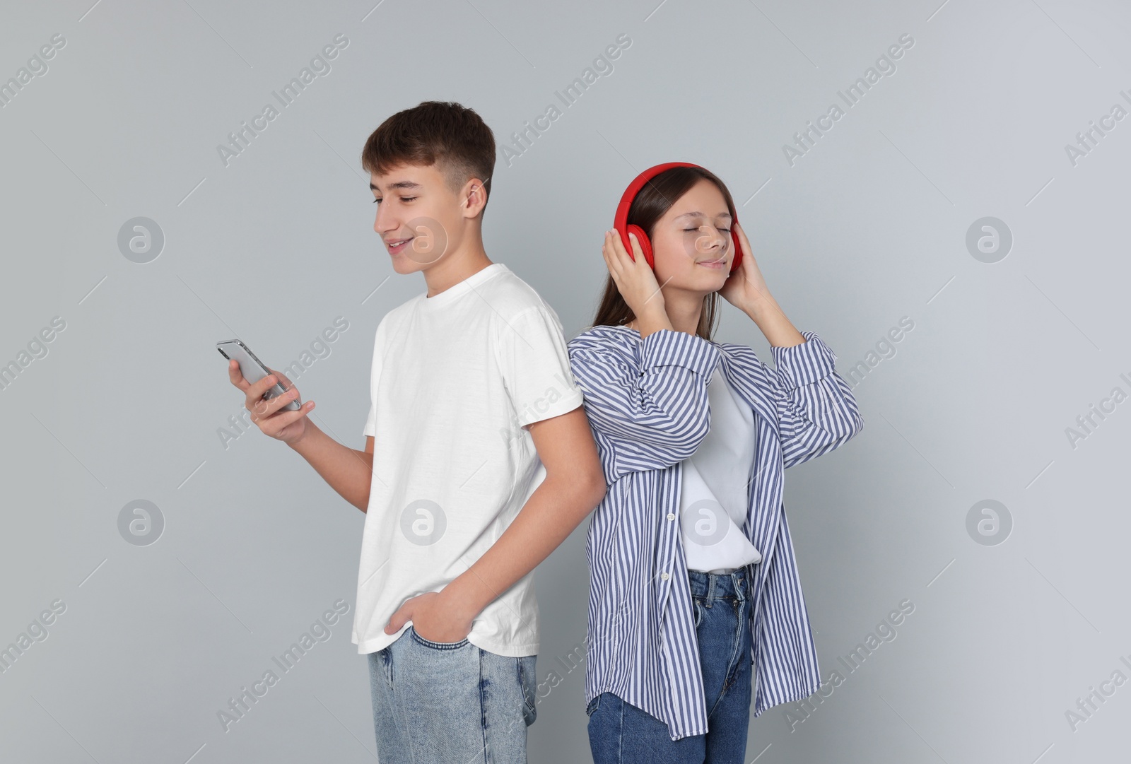 Photo of Teenage boy using smartphone and girl with headphones on light grey background