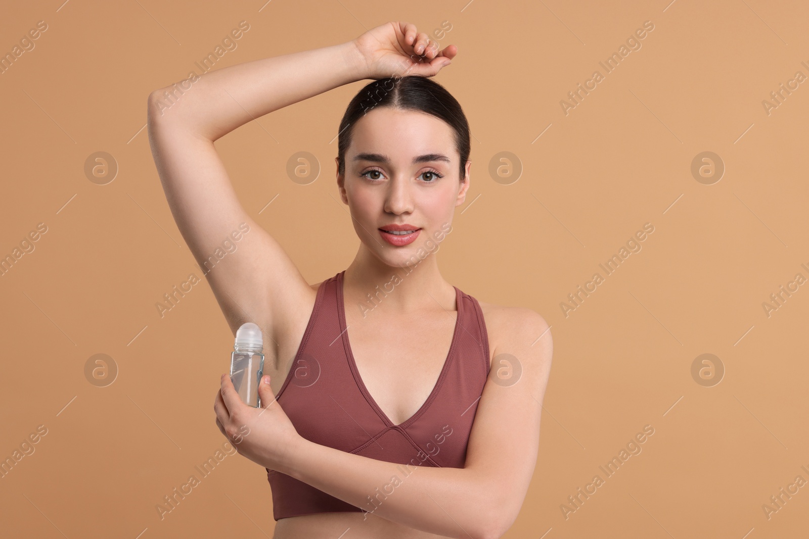 Photo of Beautiful woman applying deodorant on beige background