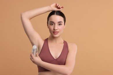 Beautiful woman applying deodorant on beige background