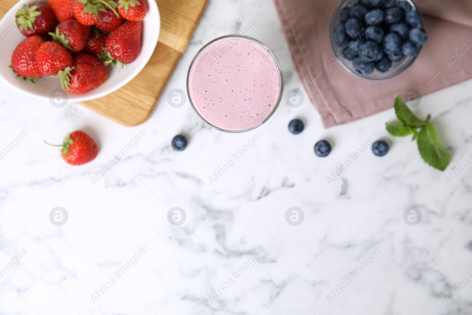 Photo of Tasty milk shake and berries on white marble table, flat lay. Space for text