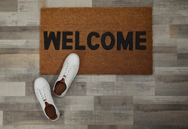 Photo of Pair of stylish white sneakers and doormat on floor, flat lay