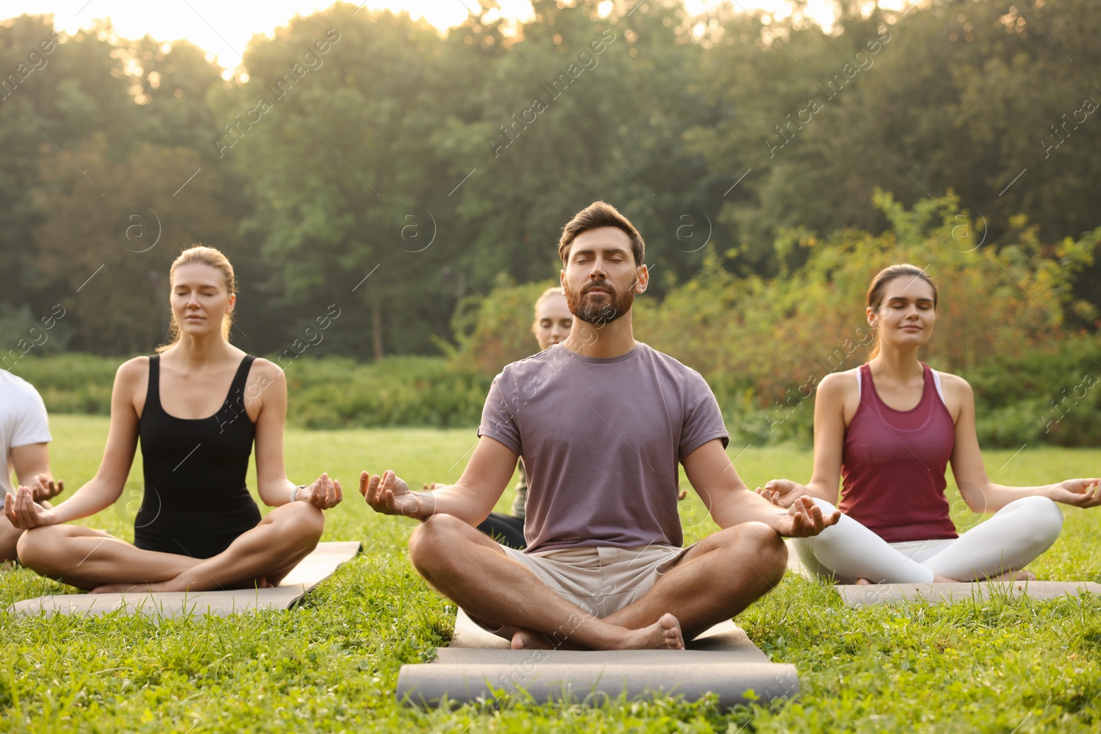 Photo of Group of people practicing yoga on mats outdoors. Lotus pose