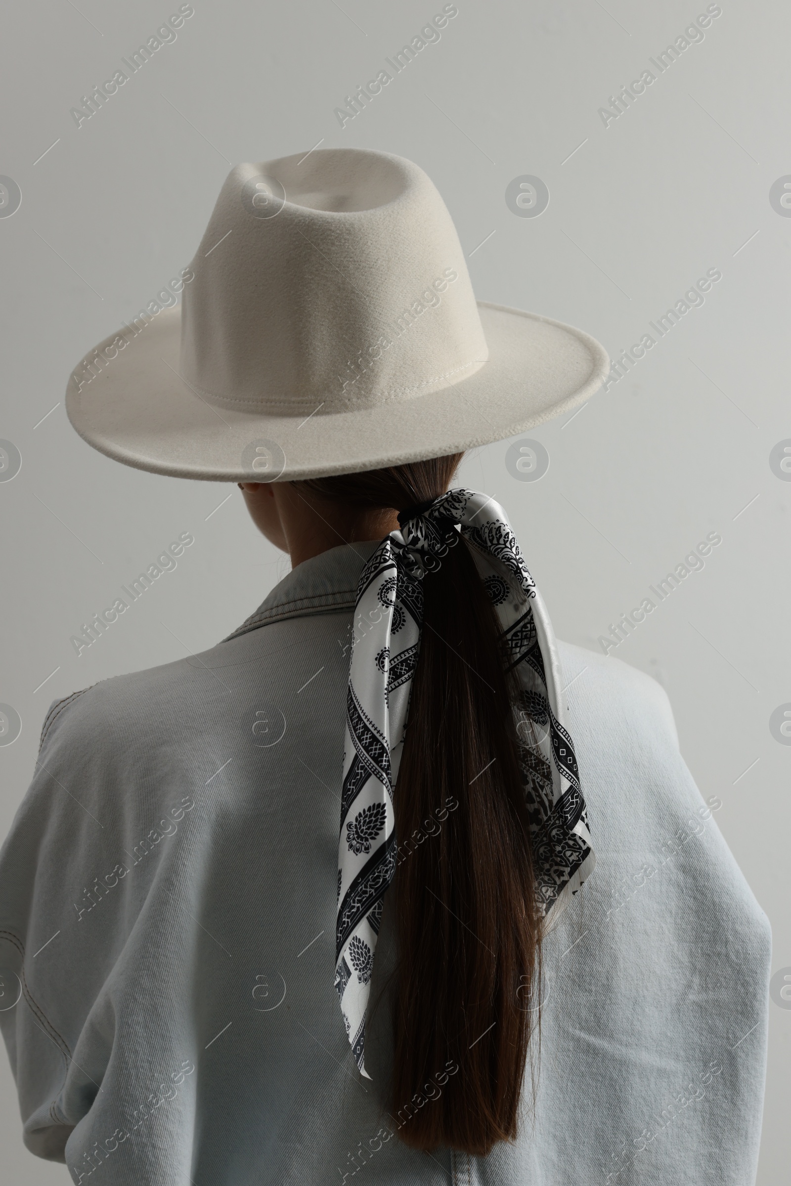 Photo of Young woman with hat and stylish bandana on light background, back view