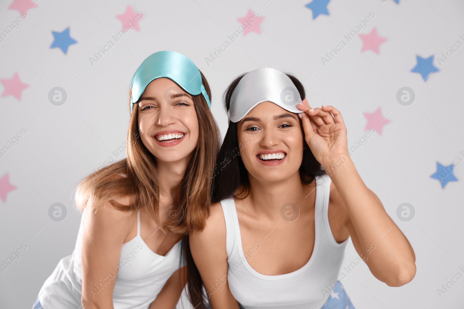 Photo of Beautiful women wearing sleeping masks on light grey background. Bedtime