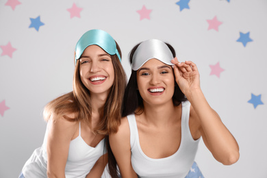 Photo of Beautiful women wearing sleeping masks on light grey background. Bedtime