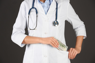 Photo of Doctor putting bribe into pocket on black background, closeup. Corruption in medicine