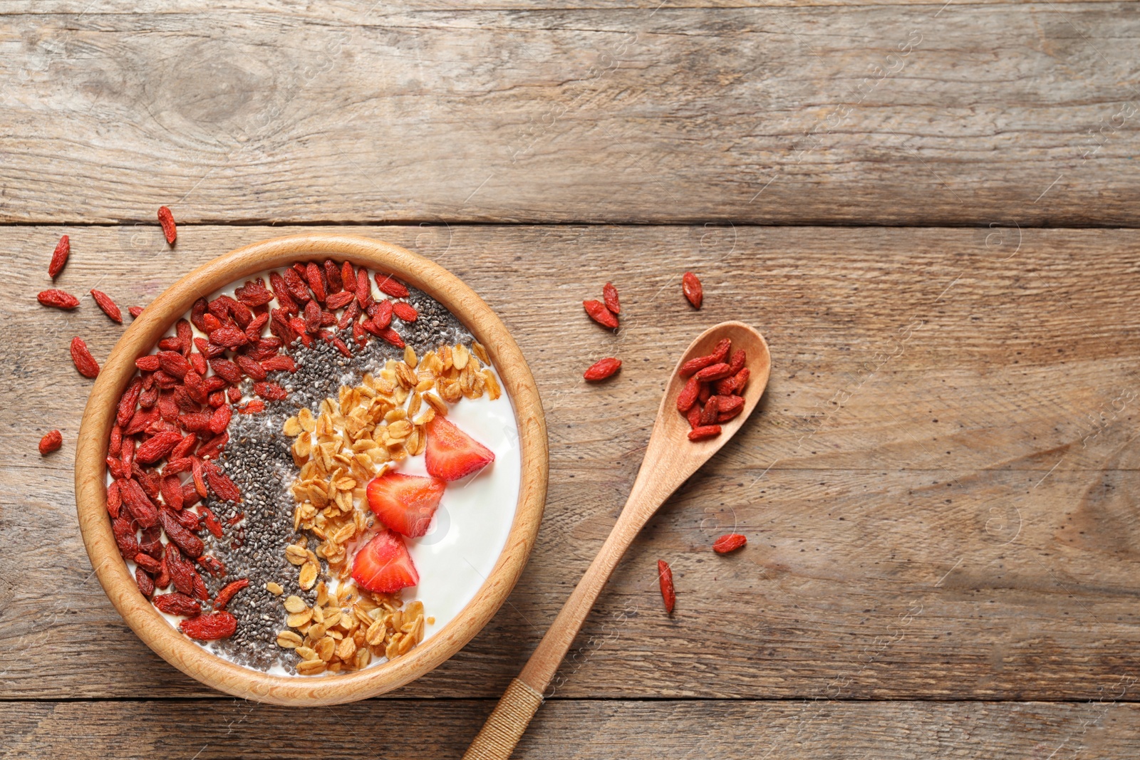 Photo of Smoothie bowl with goji berries and spoon on wooden table, flat lay. Space for text