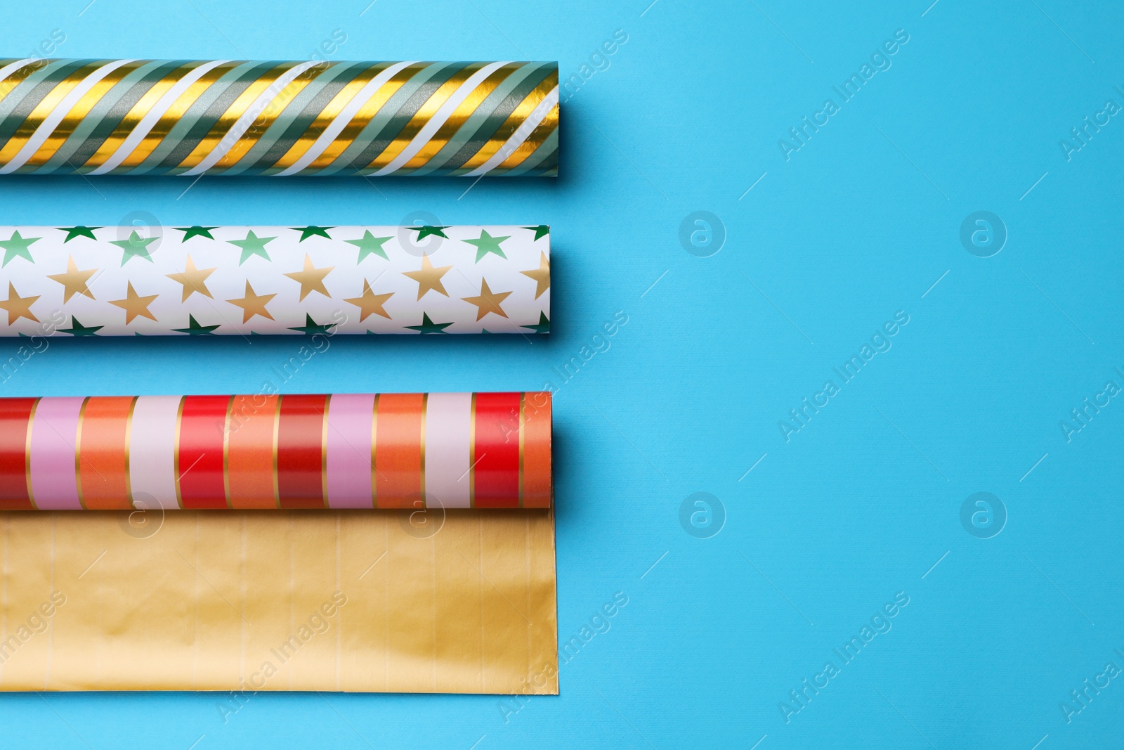 Photo of Different colorful wrapping paper rolls on light blue background, flat lay. Space for text