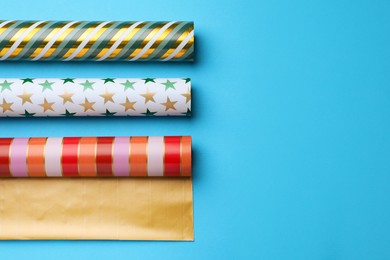Photo of Different colorful wrapping paper rolls on light blue background, flat lay. Space for text