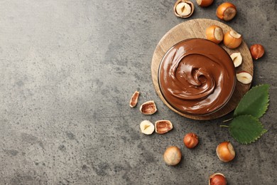 Photo of Tasty chocolate hazelnut spread and nuts on grey table, flat lay. Space for text