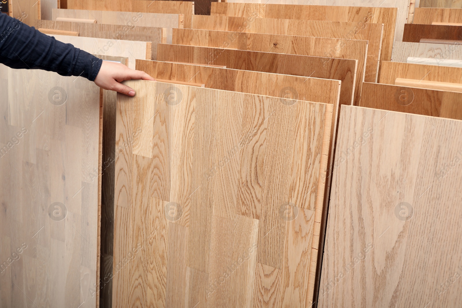 Photo of Man choosing wooden flooring among different samples in shop, closeup