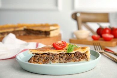 Photo of Piece of delicious pie with minced meat, tomato and basil served on light marble table, closeup