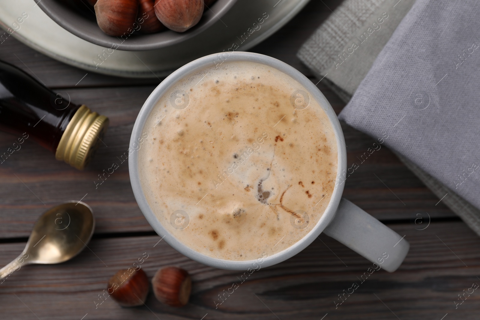 Photo of Mug of delicious coffee with hazelnut syrup on wooden table, flat lay