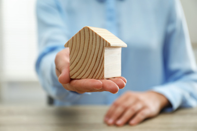 Photo of Real estate agent holding house figure at wooden table, closeup