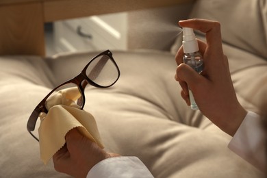 Woman cleaning glasses with cloth and spray indoors, closeup