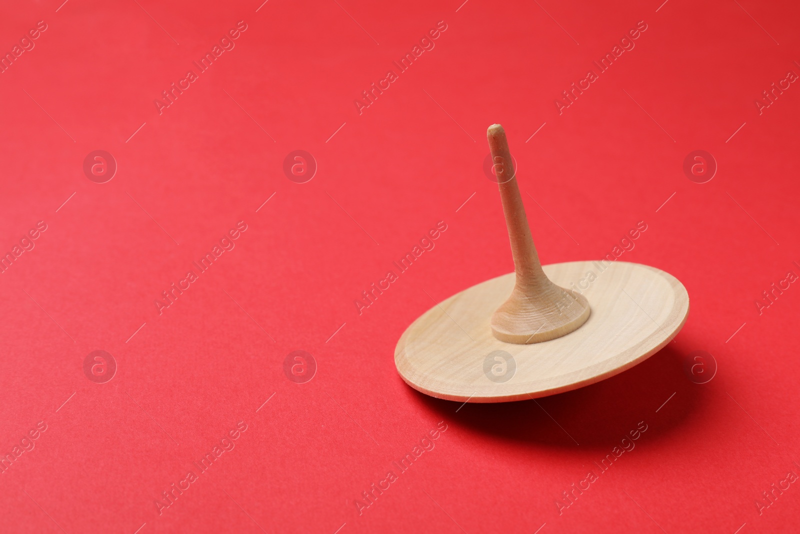 Photo of One wooden spinning top on red background, closeup. Space for text