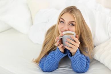 Photo of Beautiful young woman lying with cup in bed at home. Winter atmosphere