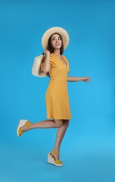 Photo of Young woman wearing dress with straw bag on light blue background