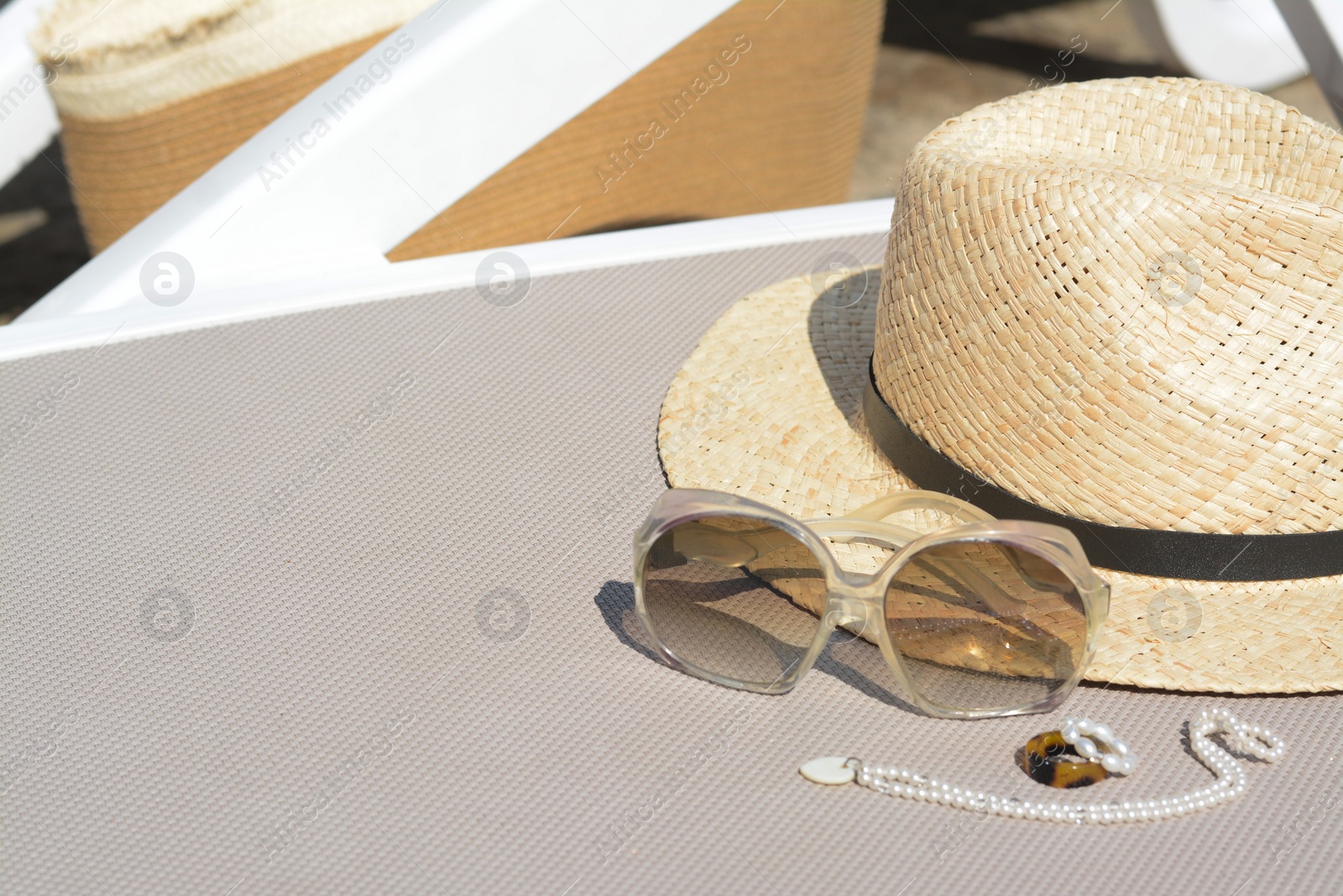 Photo of Stylish hat, sunglasses and jewelry on grey sunbed outdoors, space for text