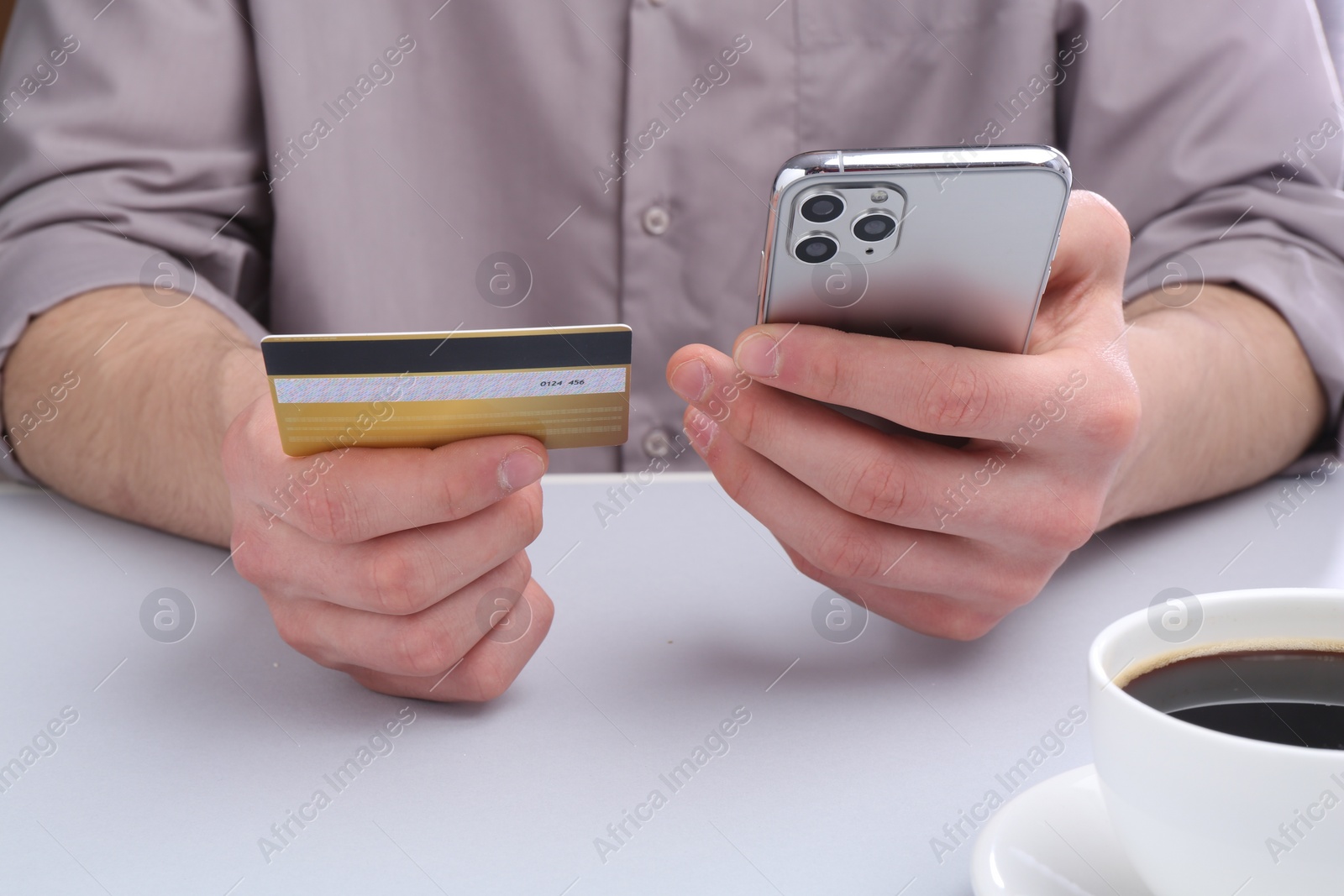 Photo of Online payment. Man with smartphone and credit card at light grey table, closeup