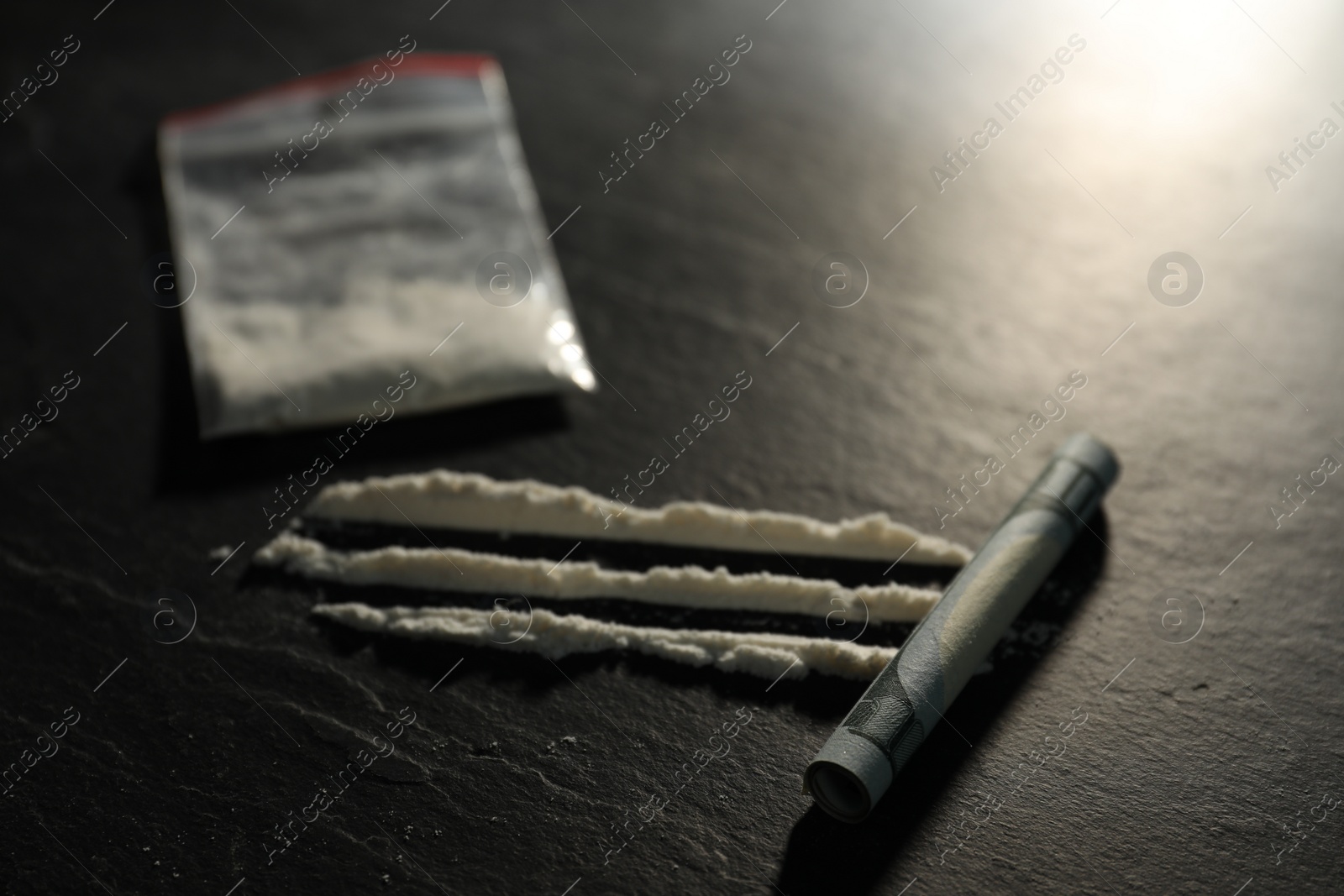 Photo of Drug addiction. Plastic bag with cocaine and rolled dollar banknote on grey textured table, selective focus