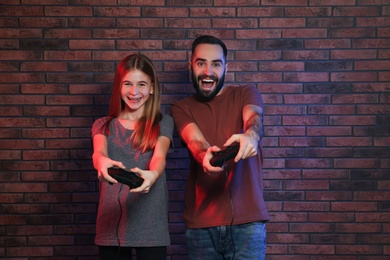 Young man and teenage girl playing video games with controllers near brick wall