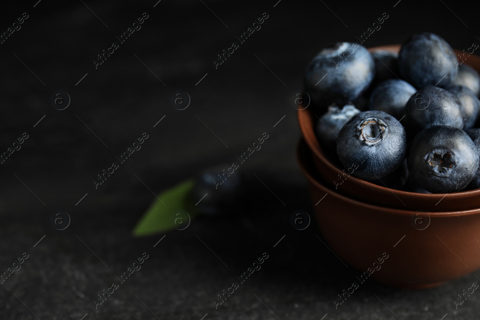 Photo of Fresh ripe blueberries in bowl on dark table, closeup. Space for text