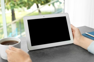 Woman holding tablet with blank screen at table. Mockup for design