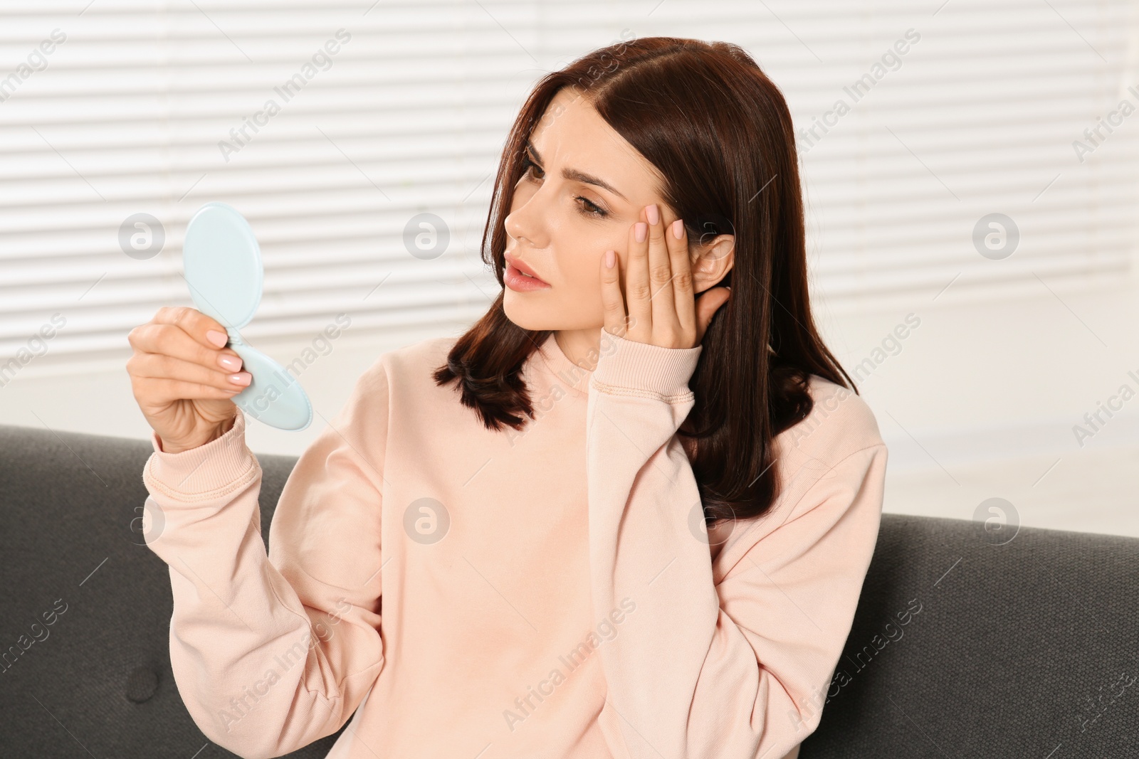 Photo of Young woman looking in mirror and touching her face indoors. Hormonal disorders