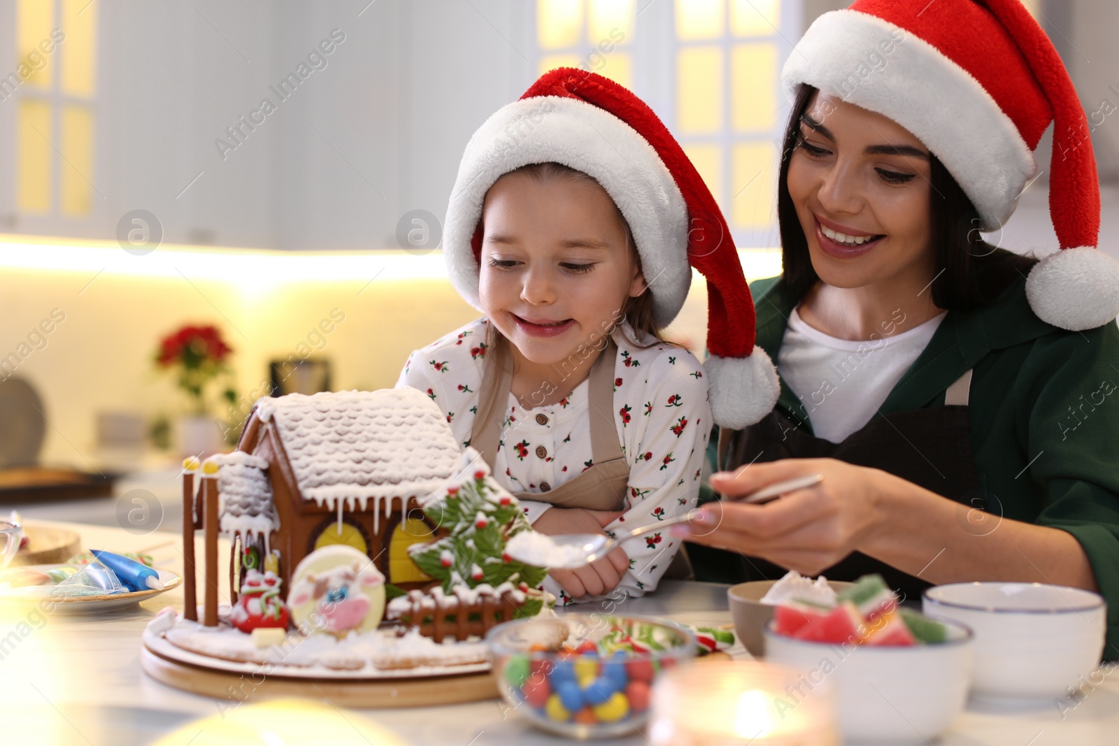 Photo of Mother and daughter decorating gingerbread house at table indoors