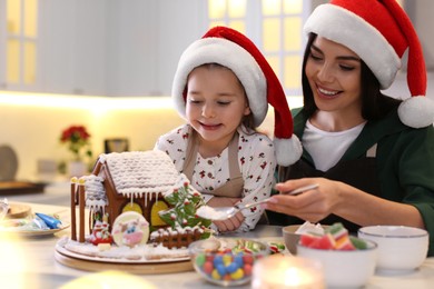 Mother and daughter decorating gingerbread house at table indoors