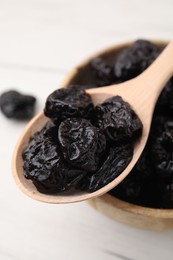 Photo of Bowl and spoon with sweet dried prunes on white table, closeup