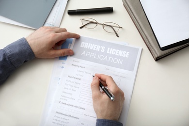 Photo of Man filling in driver's license application form at white table, top view